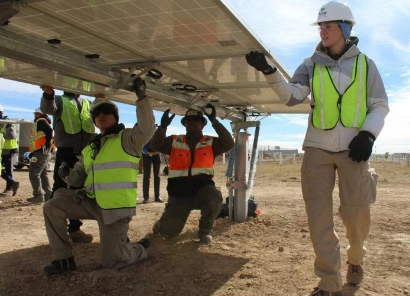 A group of workers in safety vests and hard hats install a solar panel in the ground.