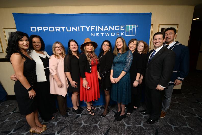 A group of professional women and men in front of an Opportunity Finance Network banner