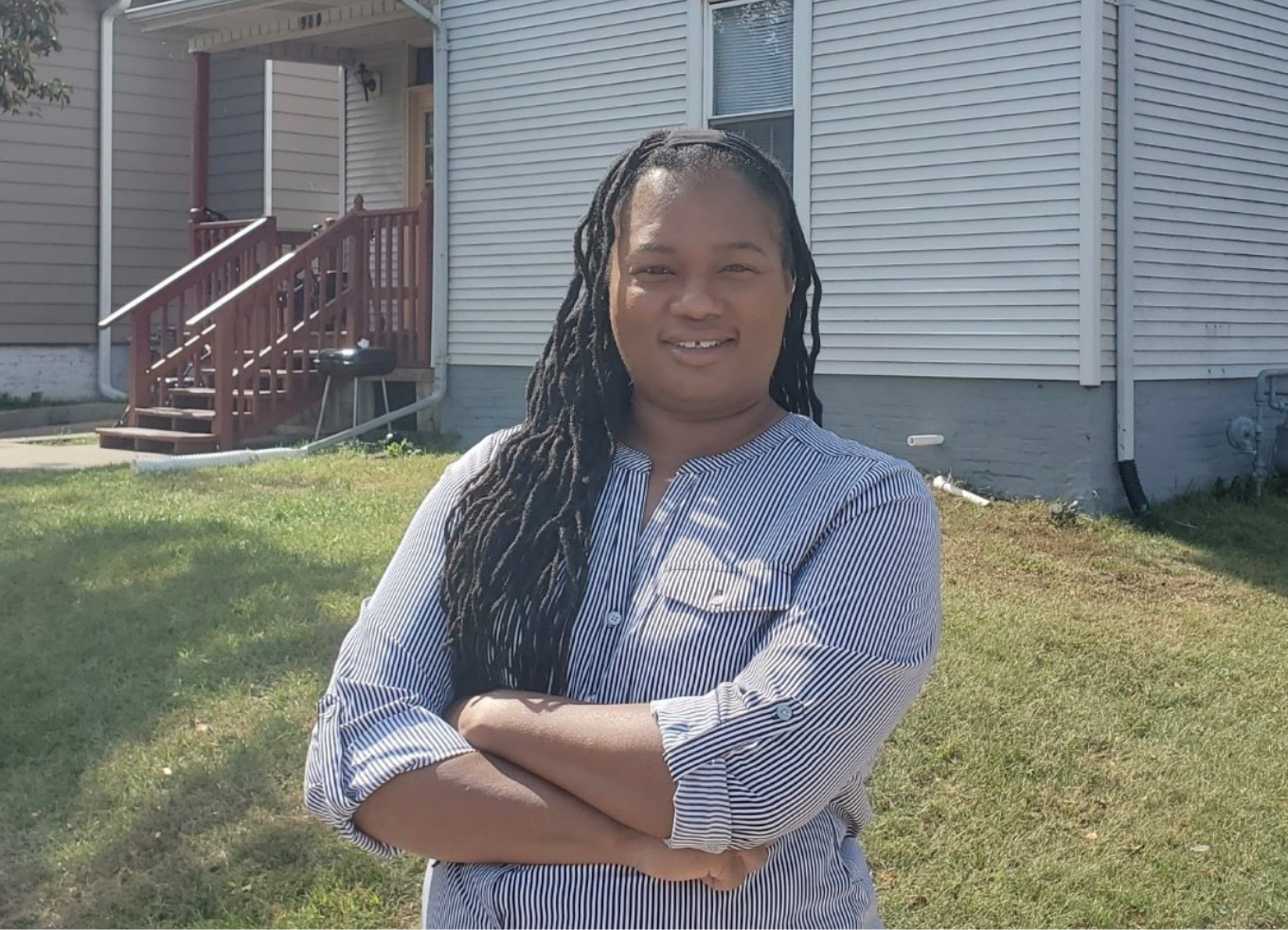 A smiling woman stands with her arms crossed in front of her new home.