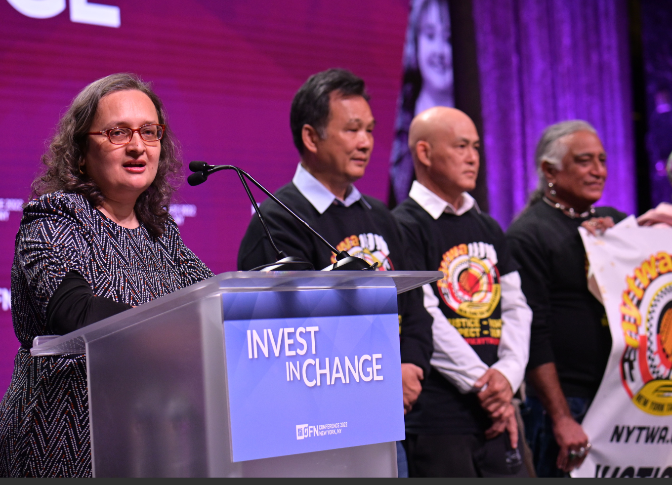 A person speaking at podium honoring a group of people standing side by side