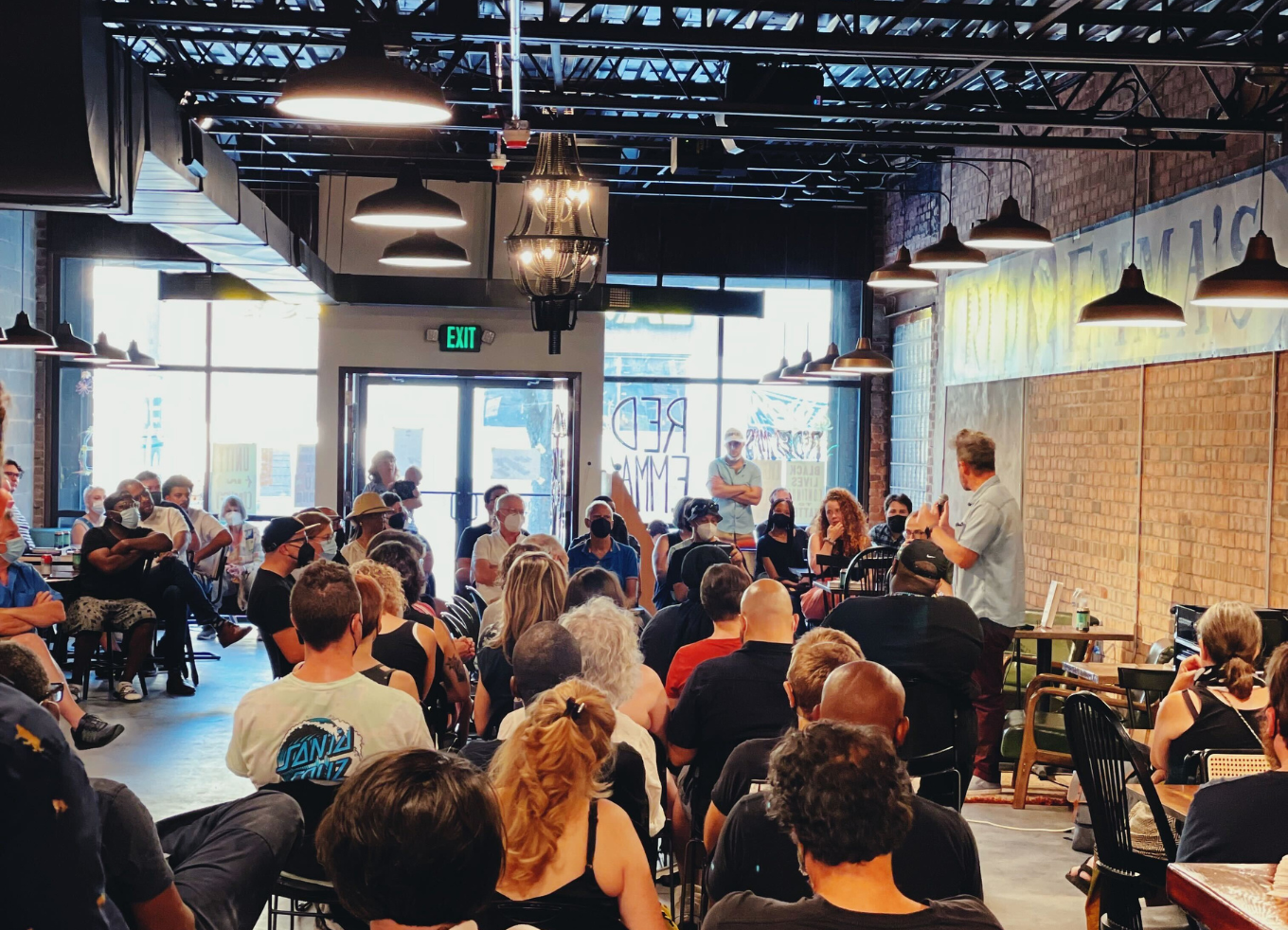 A man with a microphone addresses a crowd inside of a coffee shop.