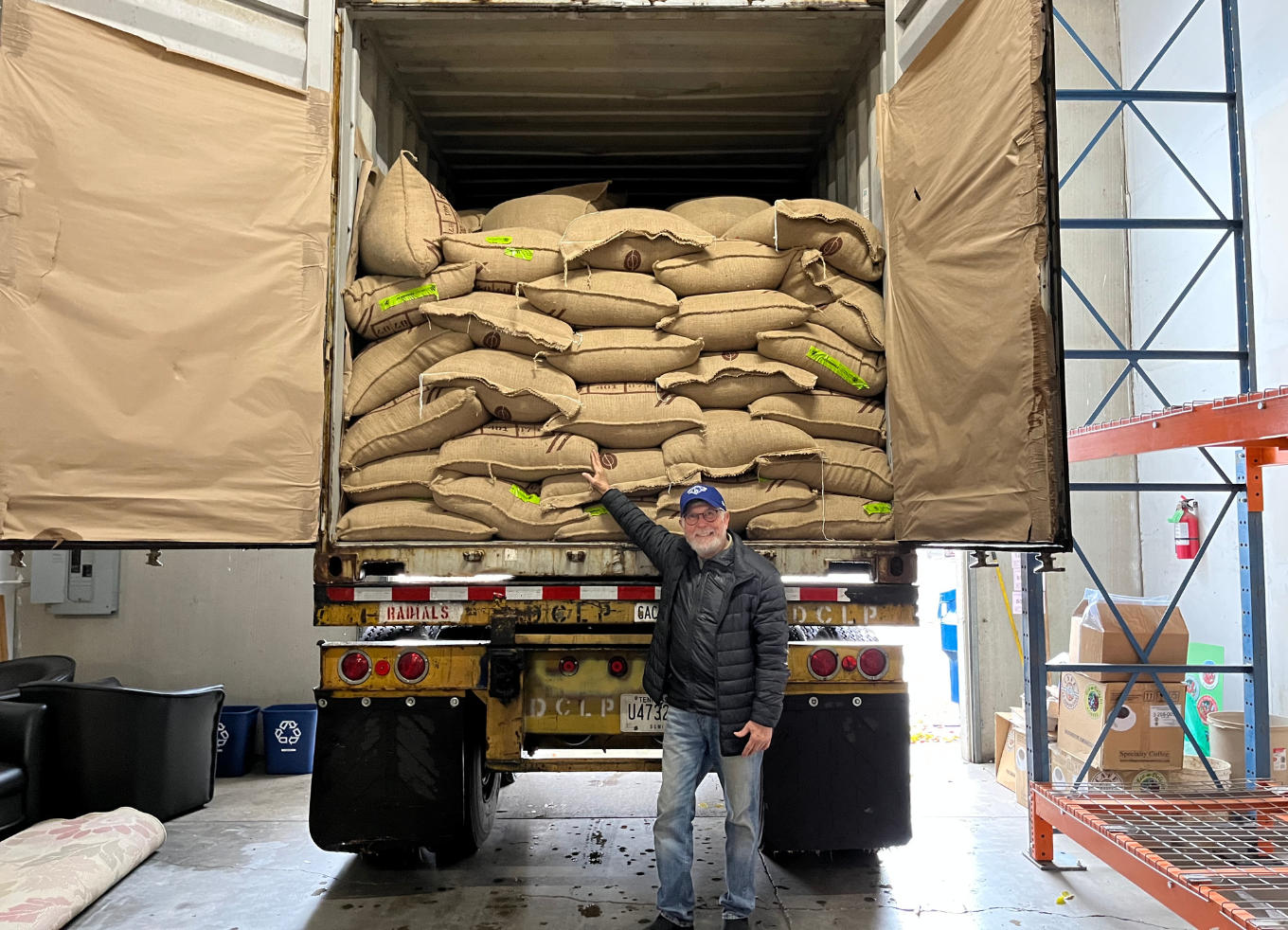 A smiling person poses with a shipping truck filled with bags