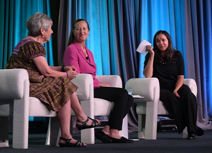 Three women sitting in chairs onstage during panel