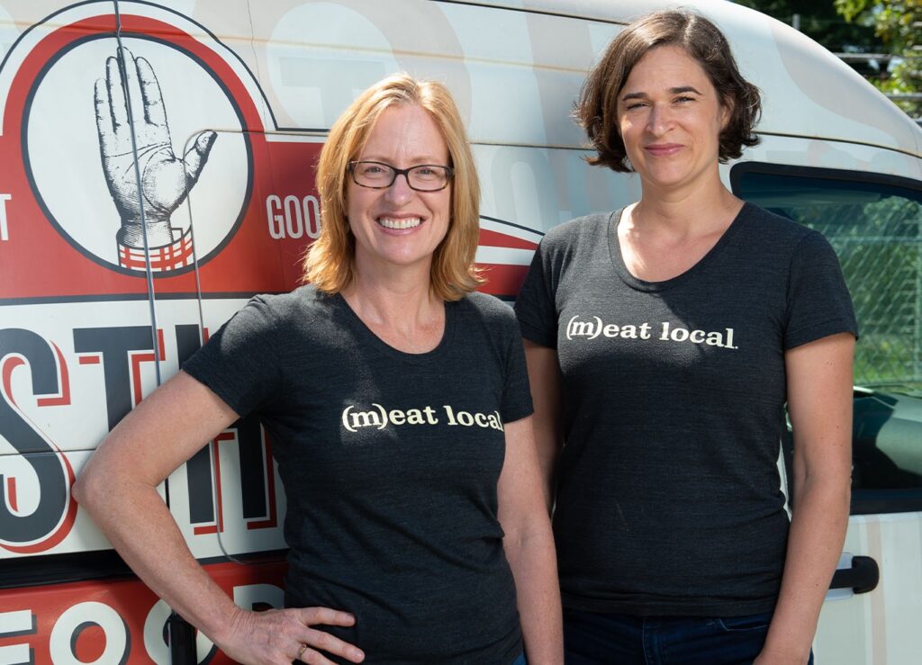 Firsthand Food founders Jennifer Curtis and Tina Levy stand smiling in front of a truck.