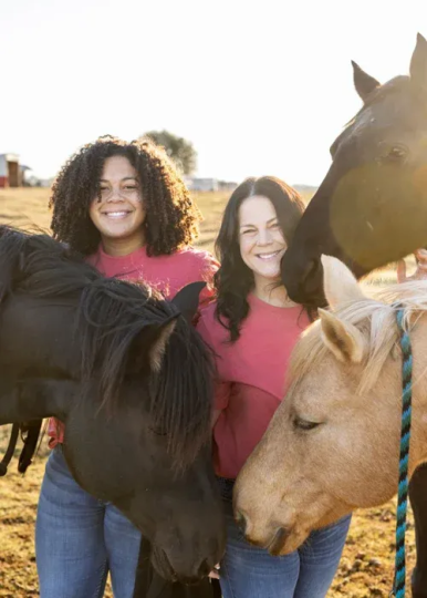 Sunset Ranch owner Jessica King and her daughter stand smiling amongst horses.