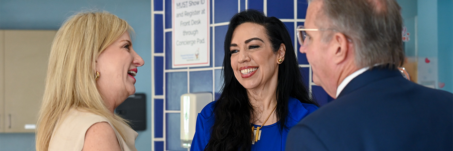 Three people talking and smiling against a blue tile and blue wall backdrop.